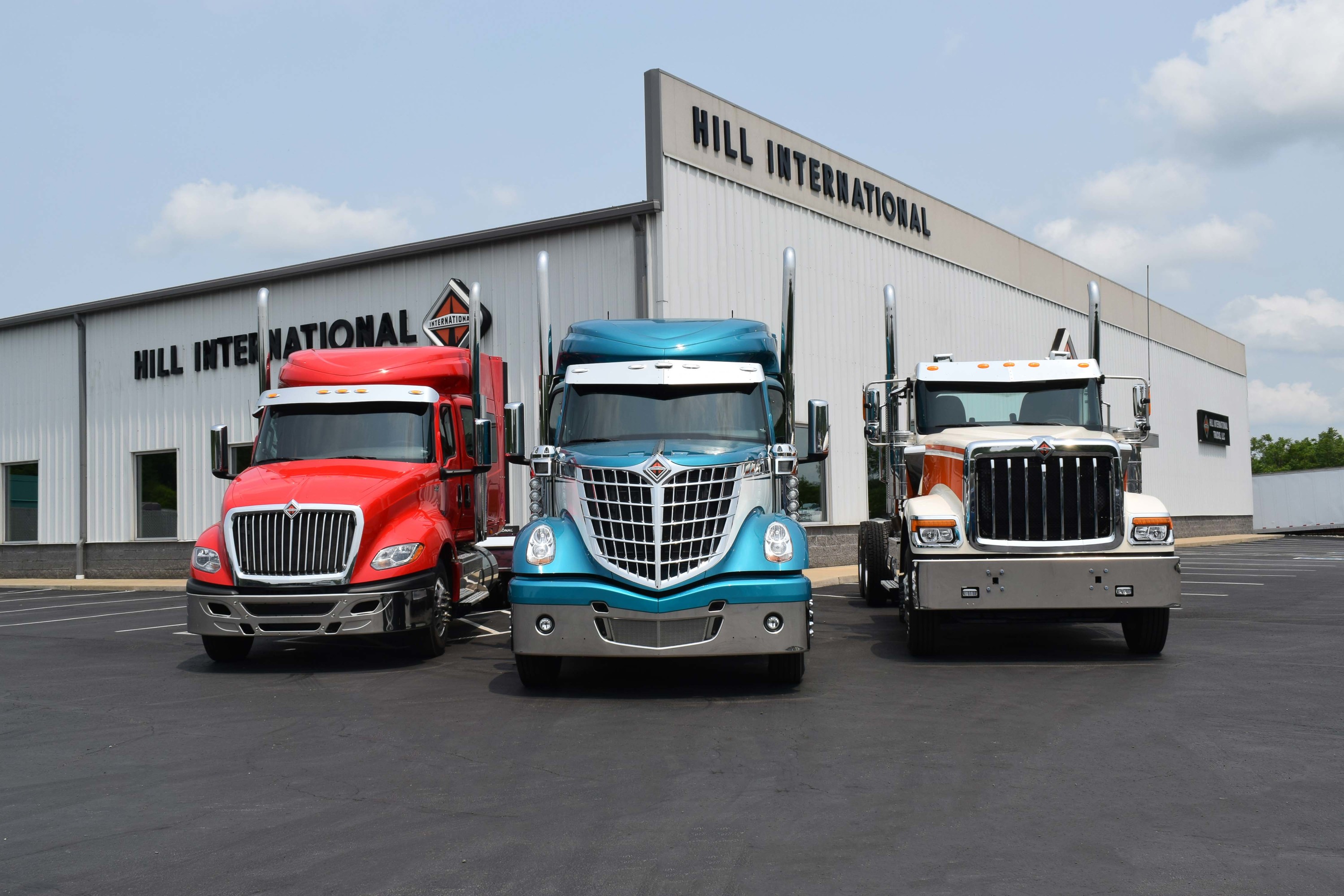 Three International® trucks parked in front of Hill International Trucks on a partly cloudy day.